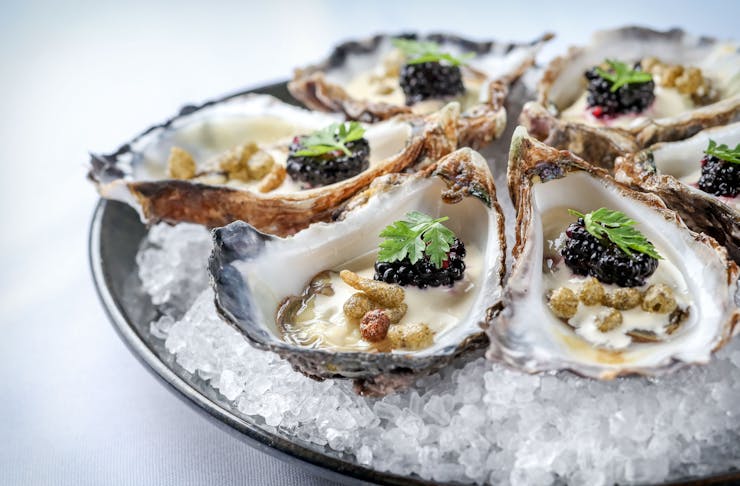 A plate of decorated oysters served on a bed of shaved ice. 