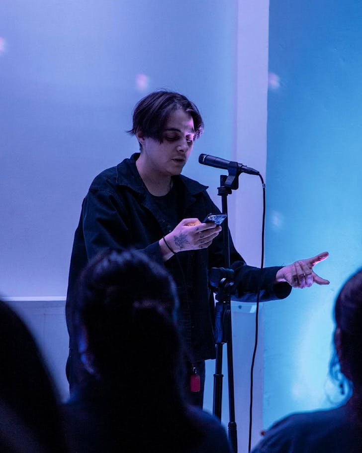 A slam poet performs in front of blue and purple lighting.