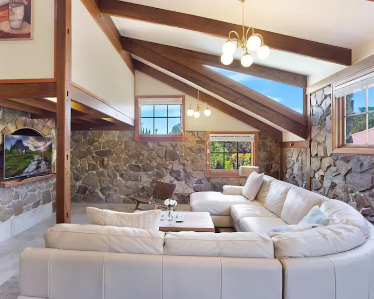 A view of the lounge with the pale L-shaped lounge and stone walls at 10 Harper Crescent Airbnb one of the best accommodation options in Narooma, NSW