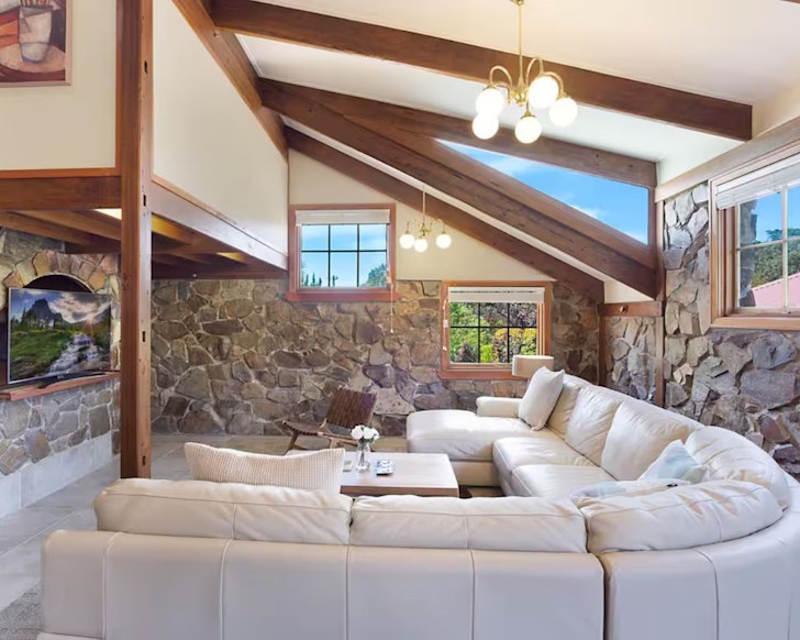 A view of the lounge with the pale L-shaped lounge and stone walls at 10 Harper Crescent Airbnb one of the best accommodation options in Narooma, NSW