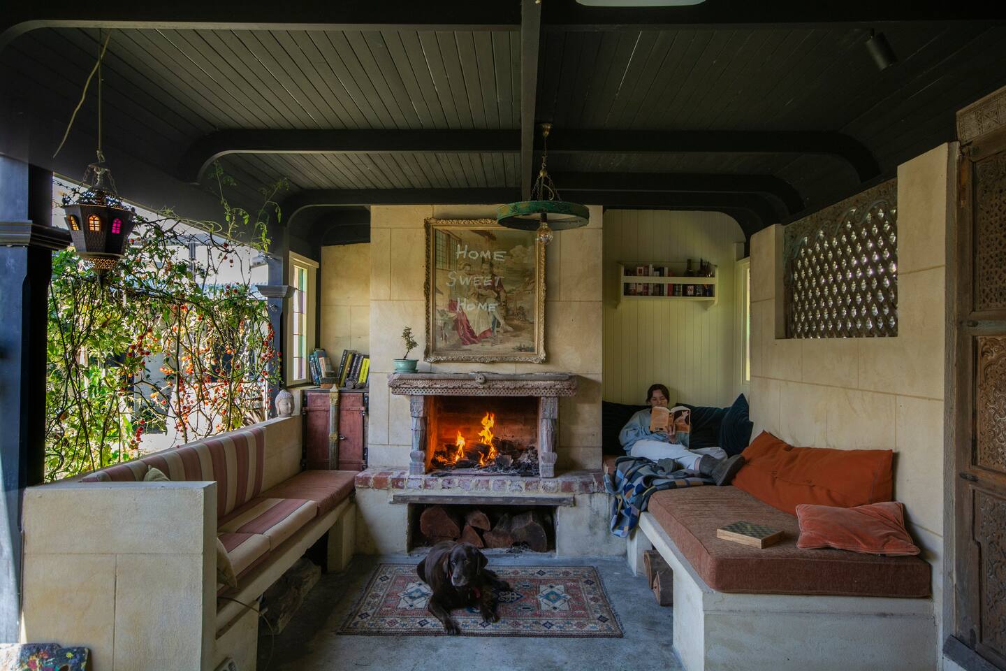 girl reads a book in an outdoor living room next to a fireplace