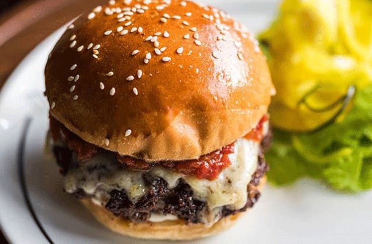 A juicy beef patty between a sesame seeded burger bun with tomato sauce and melted cheese.