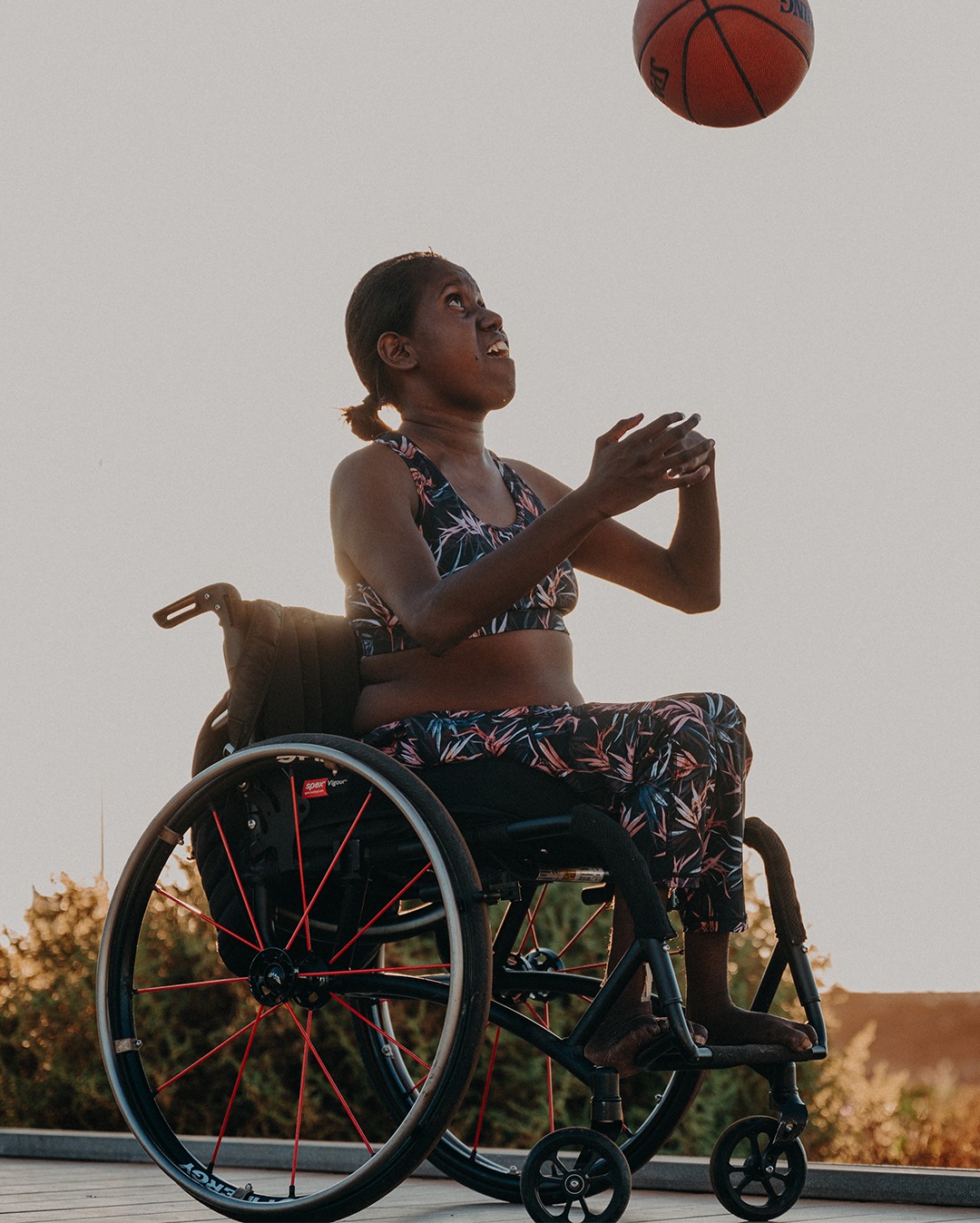 a woman in a wheelchair in activewear throwing a basketball