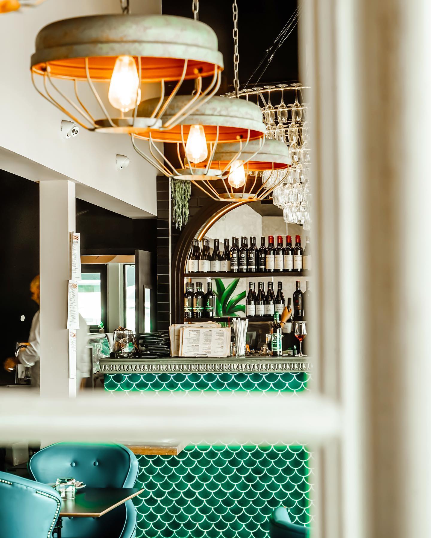 interior of a restaurant with green seating under industrial-style metal light fixtures