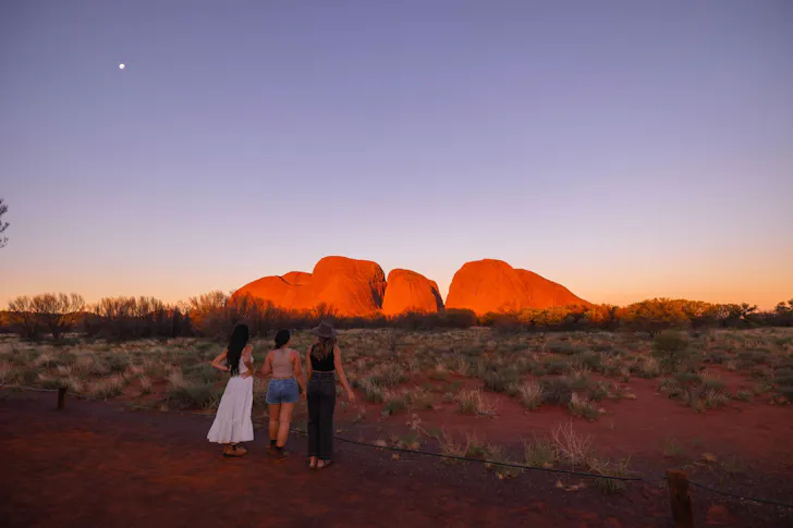 A trio of women look out to the Kata Tjuta/The Olgas at dusk