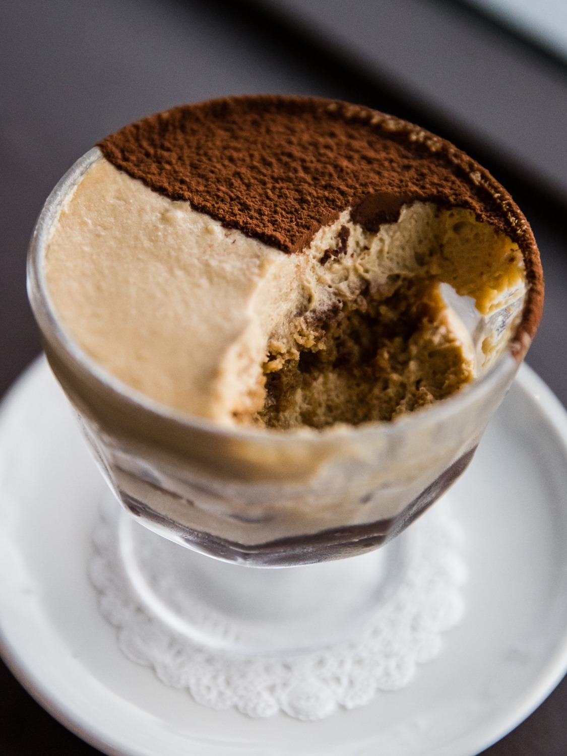 a glass cup of tiramisu with a spoonful taken out