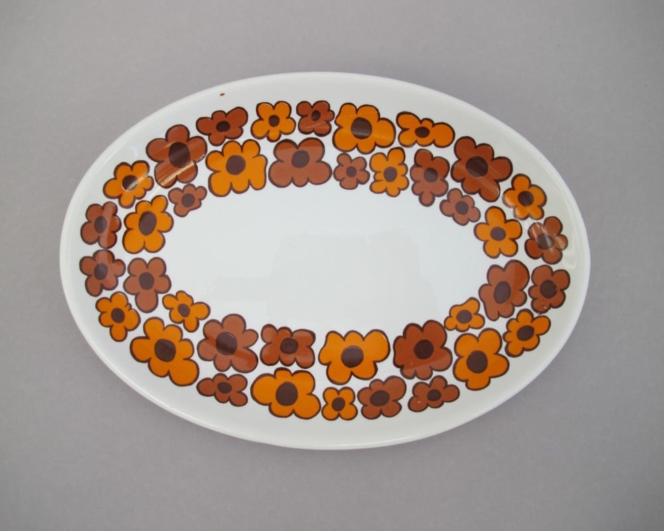 A ceramic plate decorated with joyful orange and dusky red flowers. 