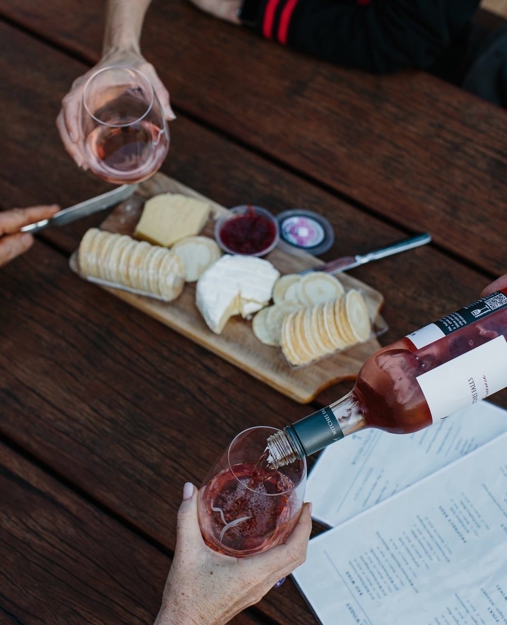 people pouring wine over a cheese board
