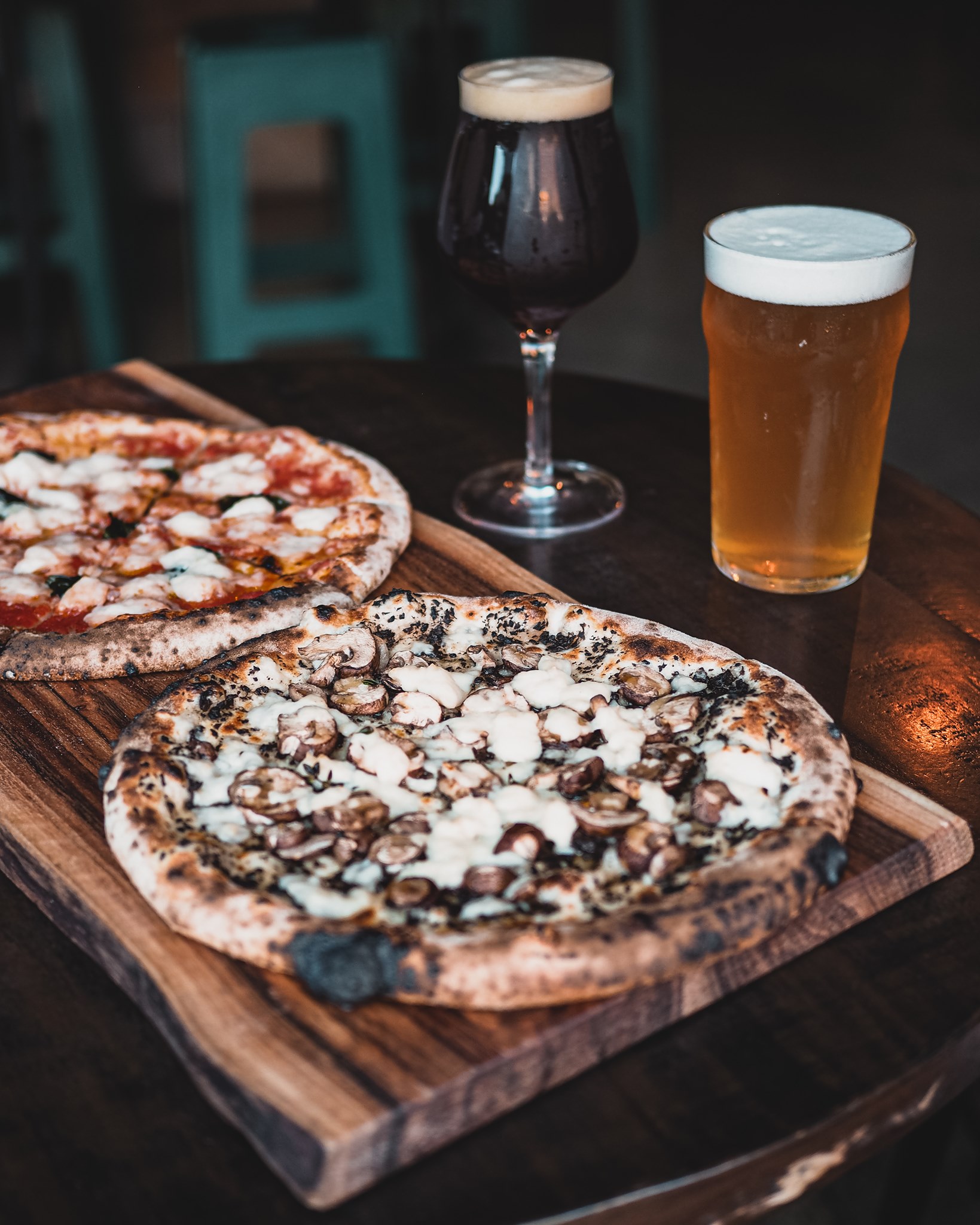 two vegan pizzas on a table with two beers