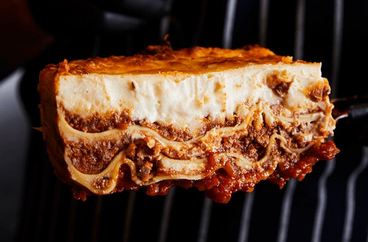A thick slab of lasagna being held up by a chef in a striped apron. 