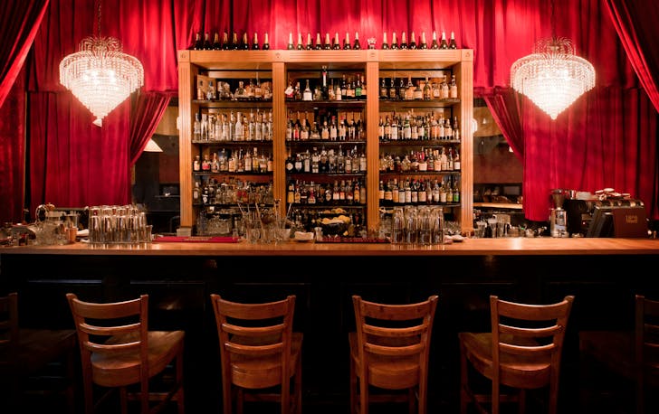 A red curtain bar, a shelves lined with bottles a top cocktail bar Melbourne. 