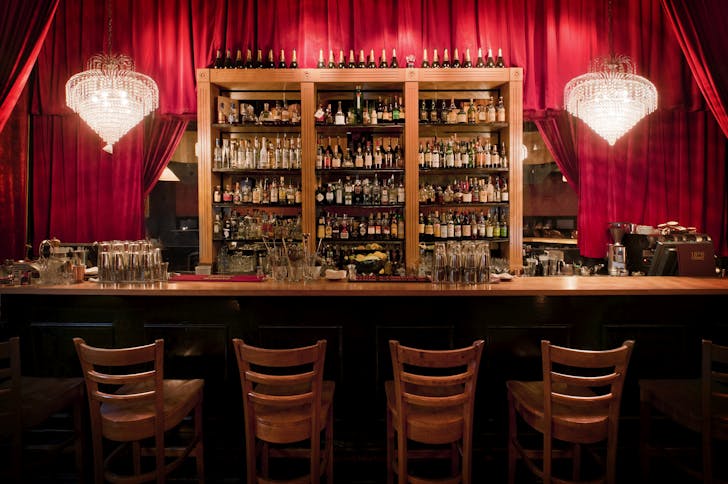 Inside one of the best bars in CBD Melbourne with red curtains and bottles.