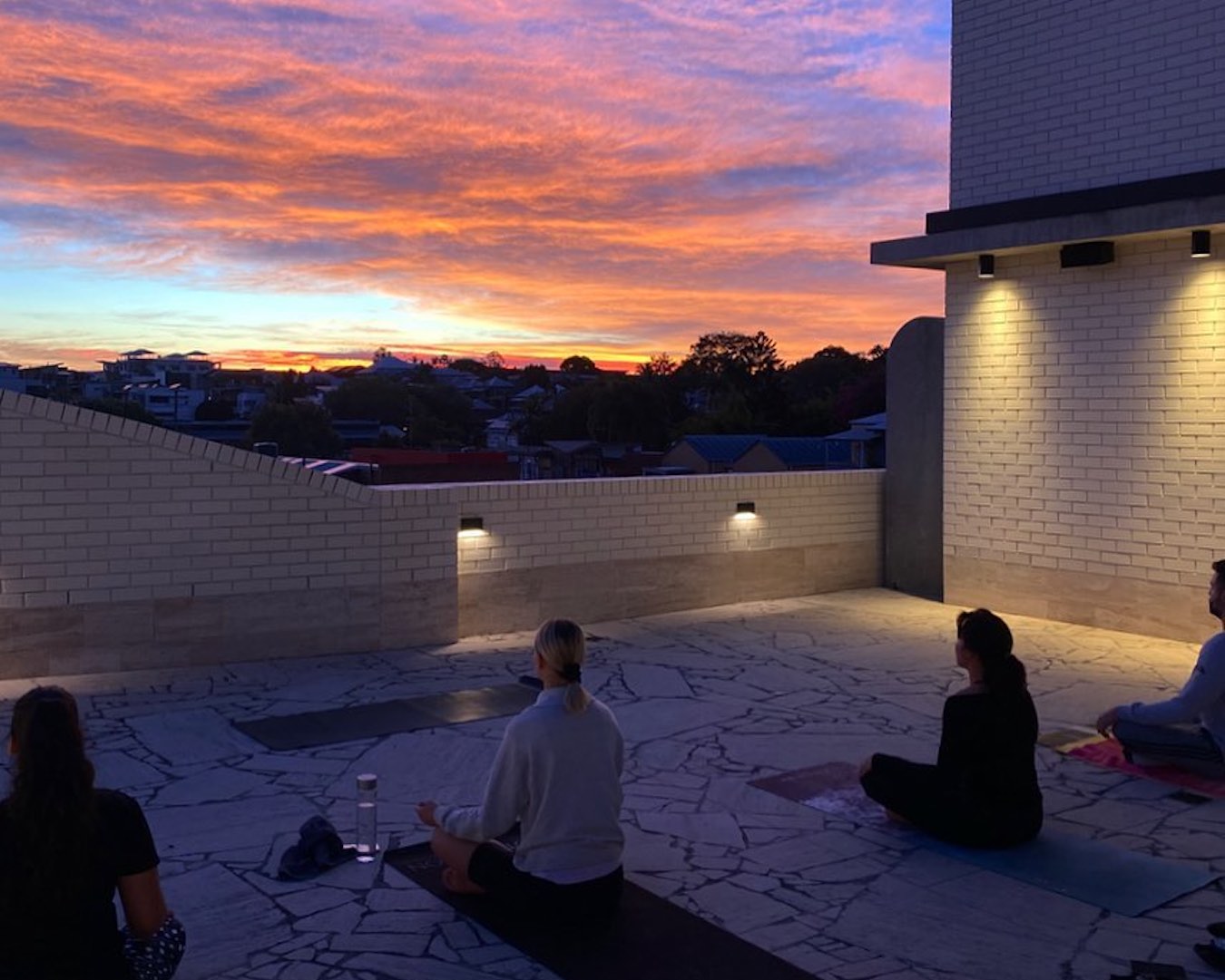 People sit cross-legged on yoga mats on a Brisbane rooftop in front of an early morning sky.