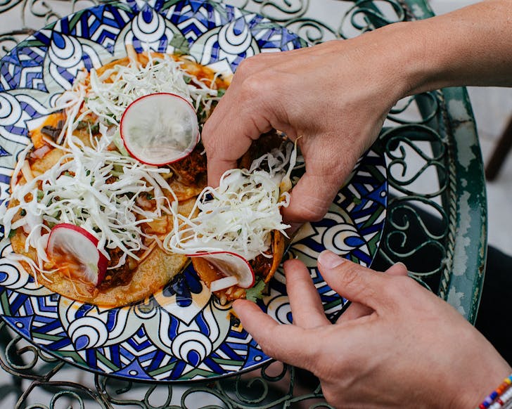 Somebody scoops up a birria taco from a blue and white patterned plate that's giving Mediterranean vibes. 