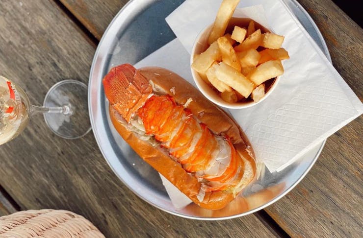 A lobster tail on a roll with chips and a glass of champagne.