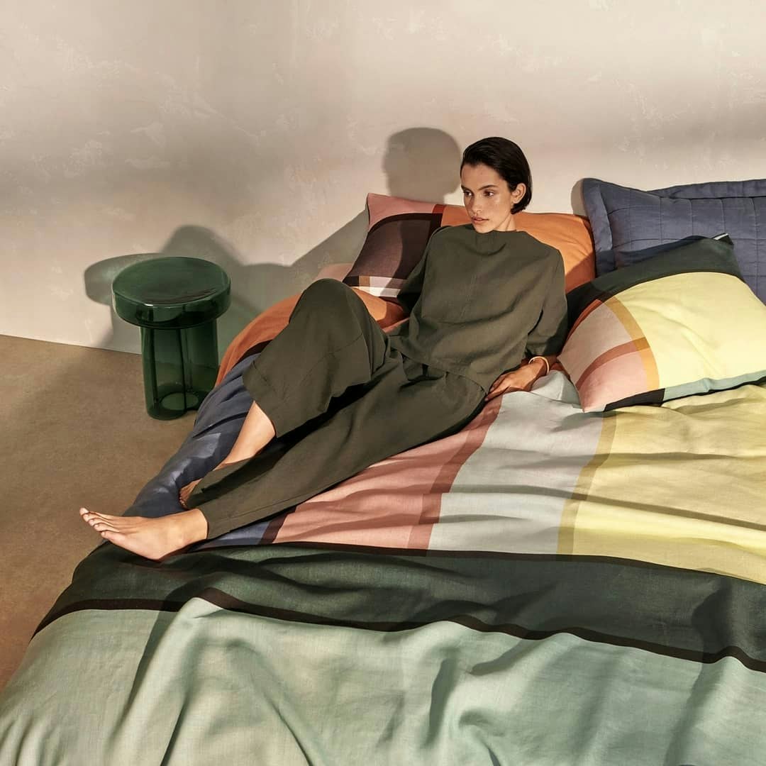 A woman lays upon a bed with a multi-coloured bed spread.