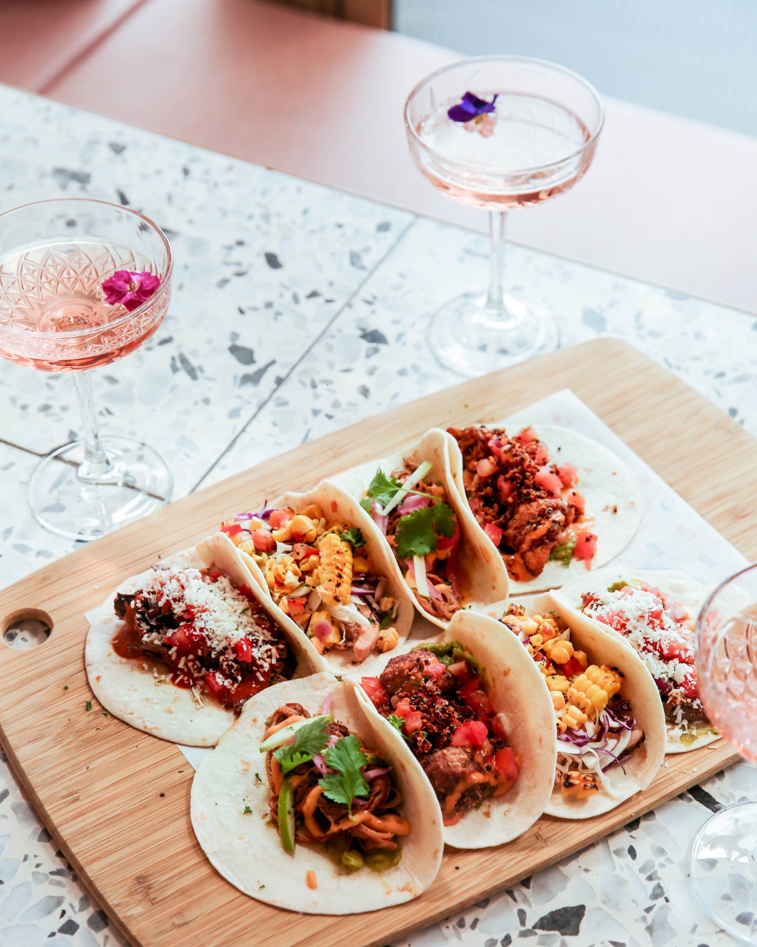 a board of different tacos with two cocktails