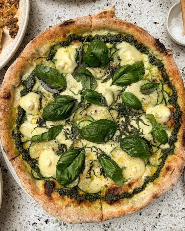 Delicious vegetarian pizza on a plate - Non Solo Pizzaâs âNeranoâ made with marinated zucchini, whipped stracchino cheese, parmesan, green pesto and lots of basil