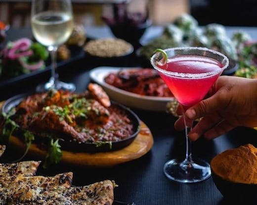 a table filled with Indian dishes and a pink cocktail