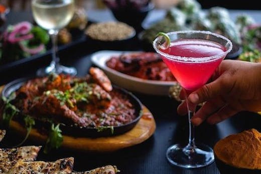 a table filled with Indian dishes and a pink cocktail