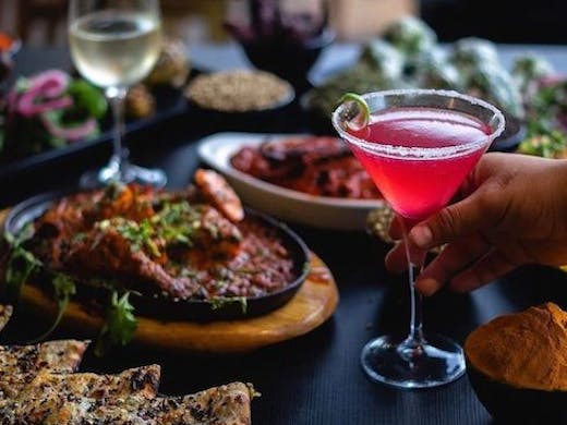 a table filled with Indian dishes and a pink cocktail