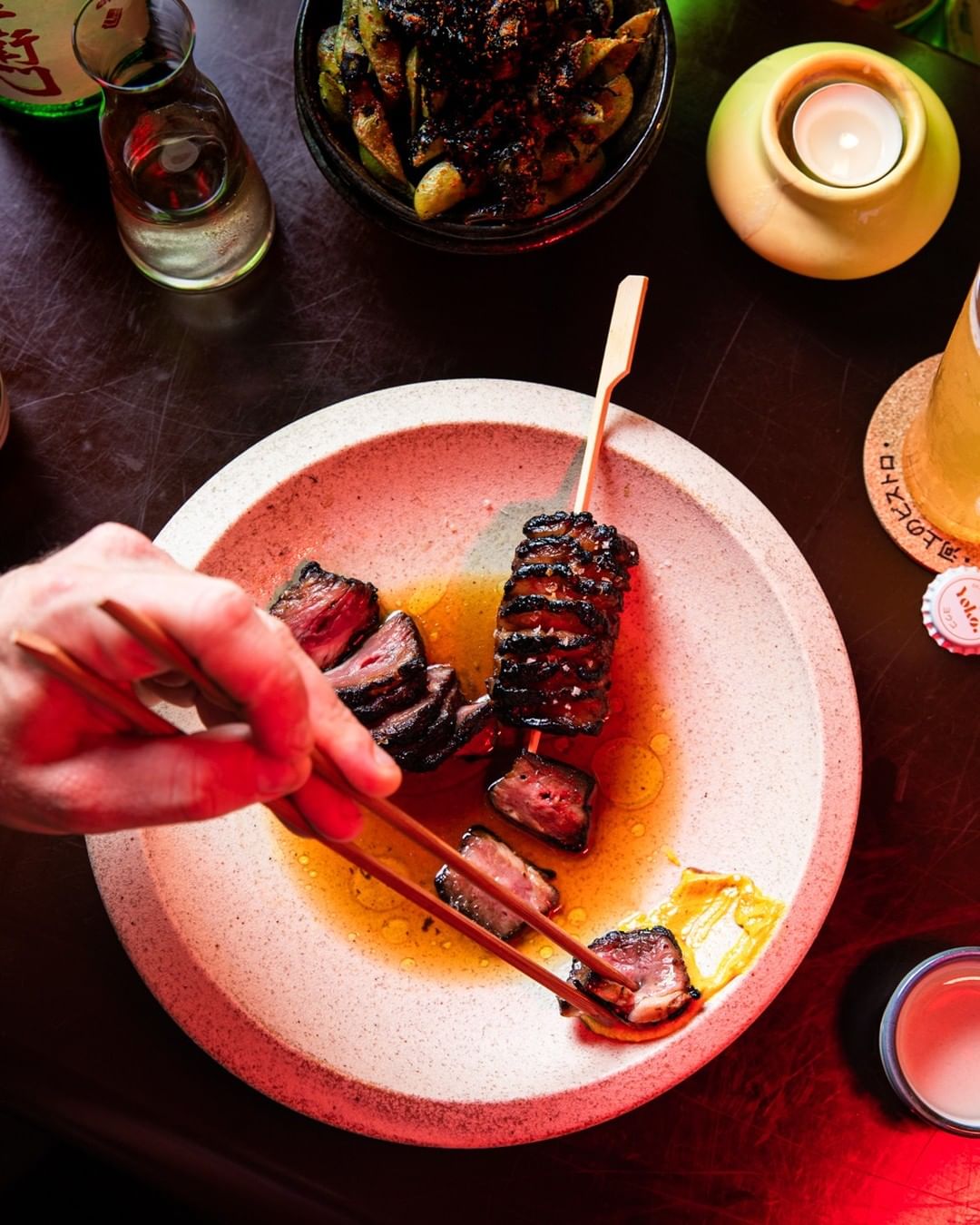 a person taking a slice of meat from a plate with chopsticks