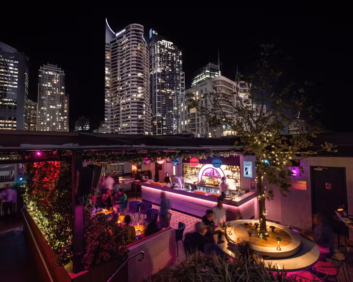 A quirky rooftop bar with bright neon lights and views of the harbour skyline.
