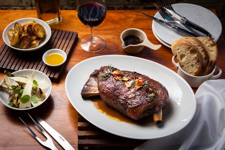 a plate of lamb shoulder surrounded by wine and sides
