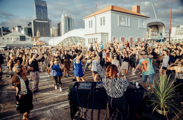 A group of people dancing at an outdoor morning rave at Shed 10, with the DJ in the foreground.