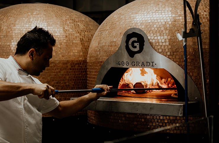 Johnny Di Francesco putting a pizza into a wood-fired oven.
