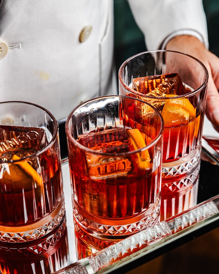 three vibrant red negronis on a silver tray at conte sydney in the cbd