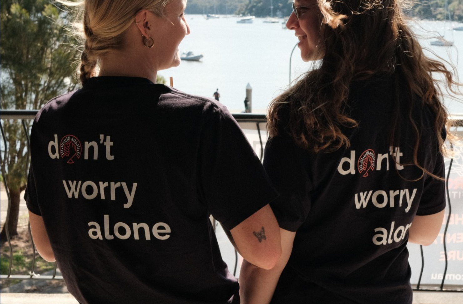 two girls face away from the camera with shirts that read 'don't worry alone'
