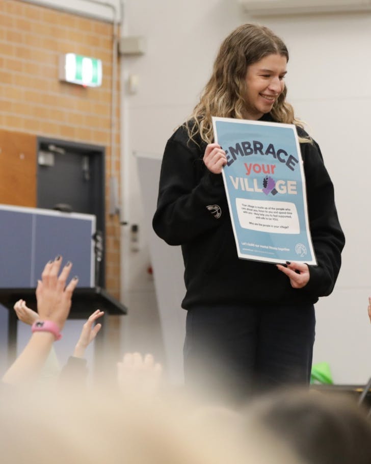 A teacher holds up a sign in front of a class that reads 'embrace your village'