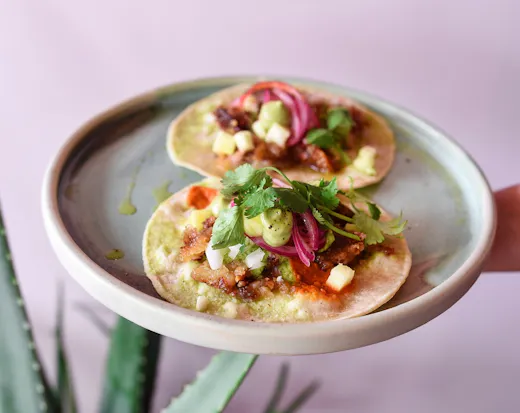 Tacos on a plate with pink background.