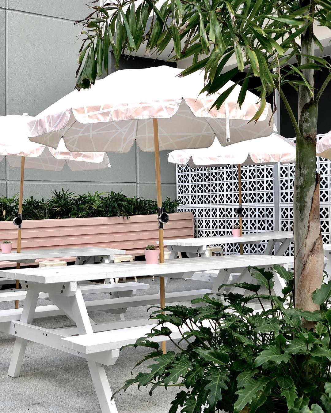 white picnic tables under pink striped umbrellas in a courtyard