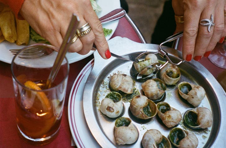 Close-up of a person using tongs and a fork to eat escargot