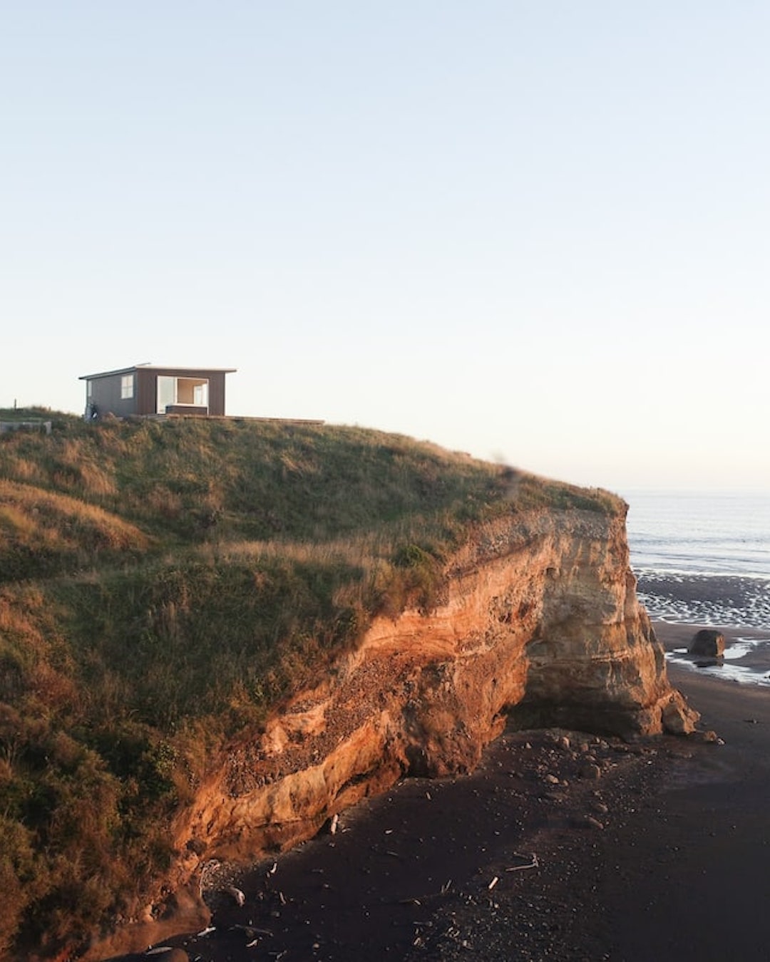 A small Airbnb cabin on a cliff above a New Zealand black sand beach