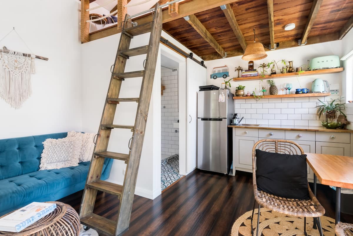 bottom level of a tiny house, with a kitchen and couch, and ladder to a loft