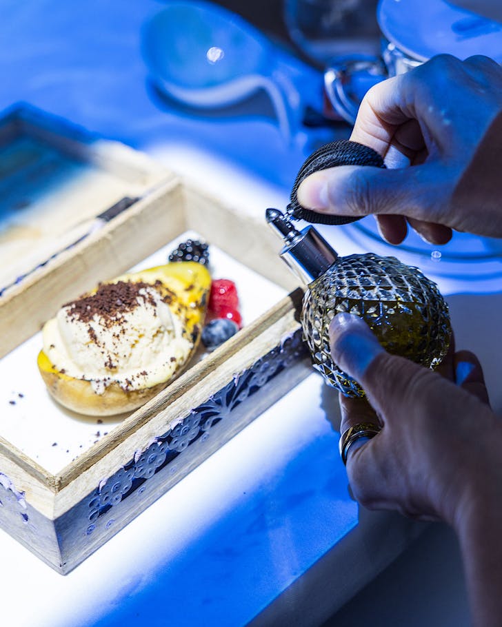 Someone sprays a vintage-style perfume onto a plate of artist-inspired food. 