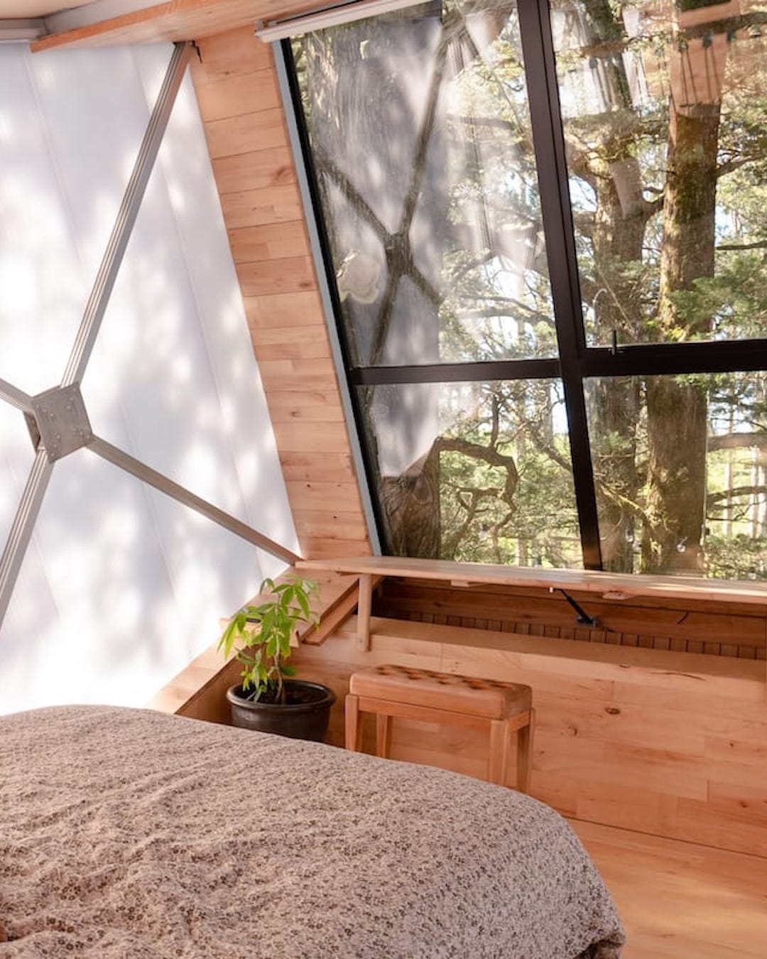 A bedroom in a wood and cloth geodesic dome looking out to trees
