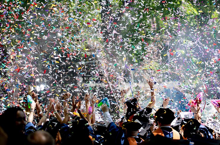 People at a festival celebrating under a cloud of confetti.
