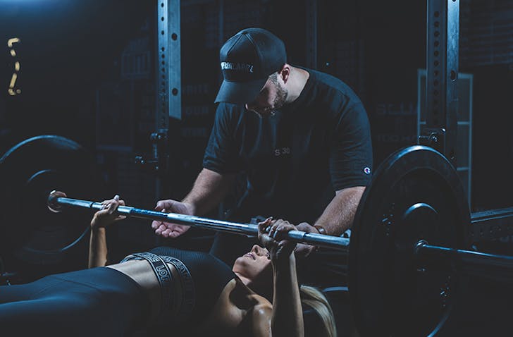 Someone spots another person as they lift weights on a bench