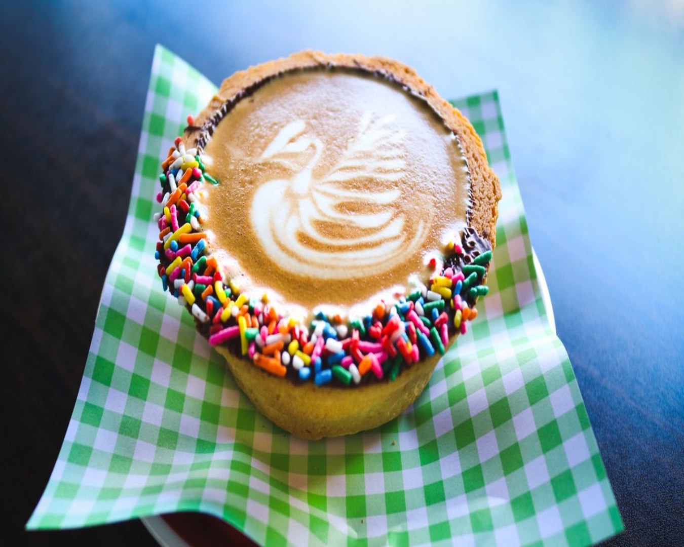 A coffee sitting in a chocolate-coated, sprinkles-topped pastry cup with a swan pattern on top. 