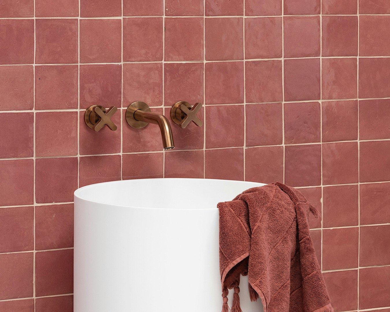 A deep red tiled sink with brass taps and a red hand towel that matches the walls. 