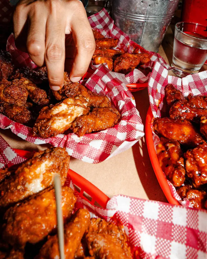 Three plates of chicken wings with a hand on top corner