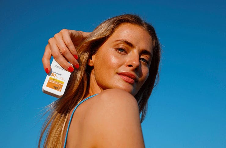 A woman holding a bottle of La Roche Posay Anthelios 50+ sunscreen.
