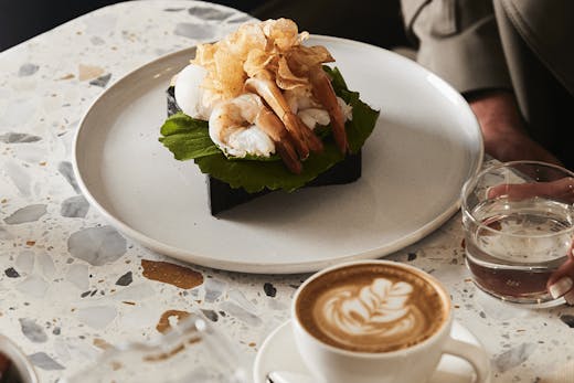 A marble table with a coffee and a prawn benedict dish.