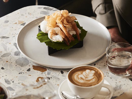 A marble table with a coffee and a prawn benedict dish.