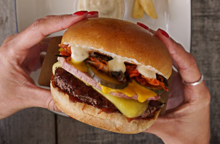 A close up of a mouth-watering burger stacked with a beef patty, gooey cheese, pickles and a glossy bun. 