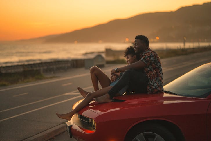 A couple sitting on a red car with a gorgeous sunset in the background. 